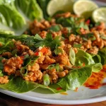['Close-up image of Spicy Chicken Lettuce Wraps, showcasing vibrant ingredients and textures.', 'Side view of juicy Spicy Chicken Lettuce Wraps arranged on a plate with fresh herbs.', 'Detailed shot of Spicy Chicken Lettuce Wraps, highlighting ground chicken and scallions in lettuce leaves.', 'Colorful presentation of Spicy Chicken Lettuce Wraps with lime wedges and sliced scallions.']