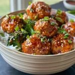 ['A close-up view of juicy Gochujang chicken meatballs on a sheet pan.', 'Side view of sticky Gochujang chicken meatballs with green onions and broccoli.', 'Succulent chicken meatballs coated in red Gochujang sauce, garnished with sesame seeds.', 'Glazed Gochujang chicken meatballs served with broccoli florets on a baking sheet.']