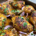 Close-up view of juicy baked curry chicken with red onion and cilantro.