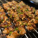 Close-up of juicy chicken skewers marinated in peanut sauce with a side of crushed peanuts.