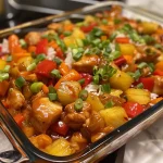 Close-up view of a Sweet and Sour Chicken Casserole topped with colorful bell peppers and pineapple chunks.