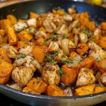 Juicy chicken and sweet potatoes in a skillet, garnished with thyme.
